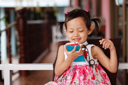 Cute little child girl playing smart phone with happy at homeの写真素材