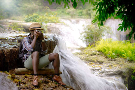 African traveler man sitting to take photo and relaxing freedom with waterfallの写真素材