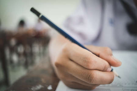 Student writing pen in hand doing exams answer sheets exercises in classroomの写真素材