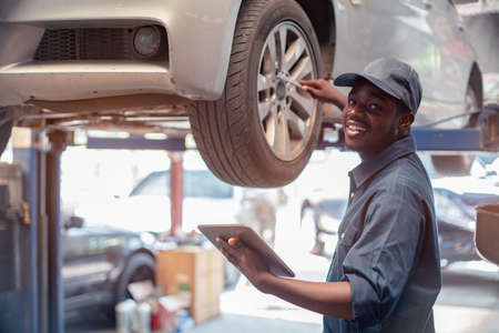 African maintenance male checking tire service via insurance system at garage with using tabletの写真素材