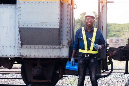 African machine engineer technician wearing a helmet, groves and safety vest is using a wrench to...