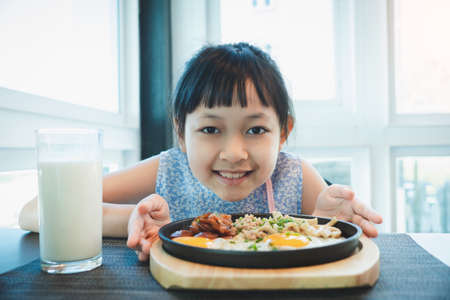 Asian little girl smiling with fried egg and fresh milk in breakfastの写真素材