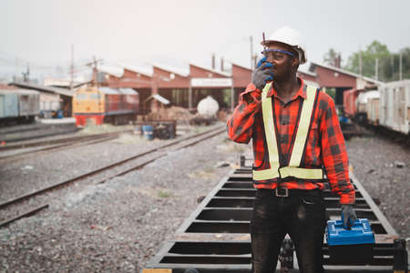 African machine engineer technician talking with walkie talkie and wearing a helmet, groves and...