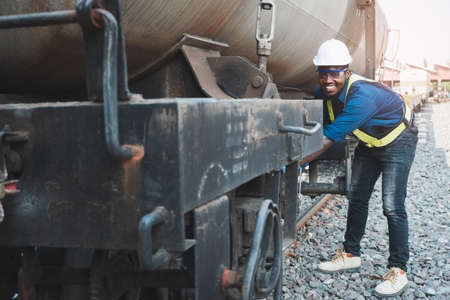 African machine engineer technician wearing a helmet, groves and safety vest is using a wrench to...