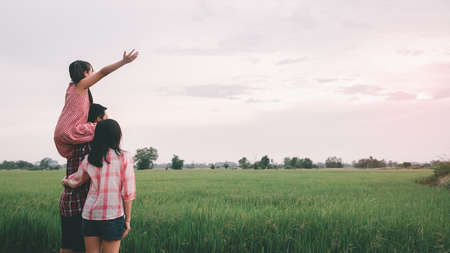 Happy asian family standing amidst rice crops at farm against sunsetの写真素材
