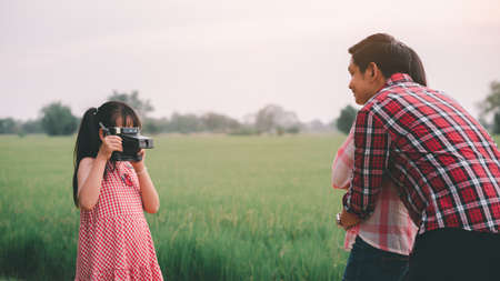 The vintage little daughter take a photo for her parents with a film camera, happily hugging each...