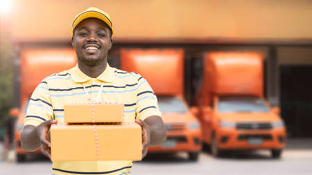 African male postal delivery courier man holding delivering package boxs in front of carの写真素材