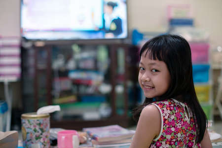 Asian little schoolgirl studying during her online lesson at home with her parent, social distance...