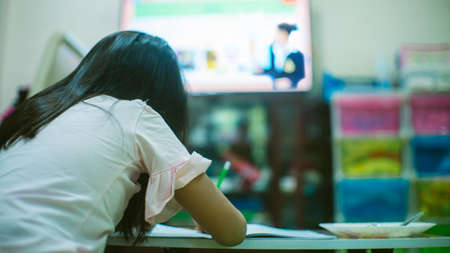 Asian little schoolgirl studying during her online lesson at home with her parent, social distance...