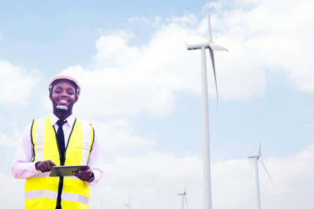 Successful african engineer windmills standing and hoding tablet with wind turbine in backgroundの写真素材