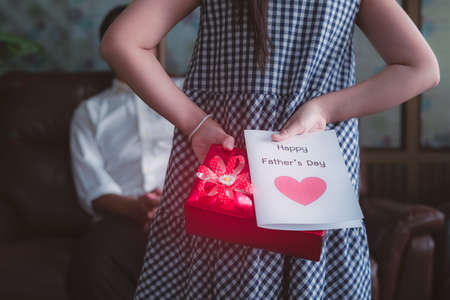 Little girl daughter holding and hiding greeting card for father behind back.Concept of Happy father's dayの写真素材