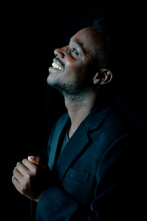 African man praying for thank god in the dark room.Low key lighting style