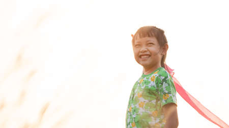 Asian little child girl is holding and smiling with a kite on meadow in summer in natureの写真素材