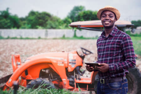 African farmer is using a tablet on the background of working tractor with a cultivator in the field.Agriculture or innovate cultivation conceptの写真素材
