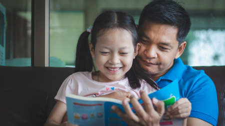 Father helping daughter to reading a book and do homework with smile and happy at home.Concept of fathers dayの写真素材
