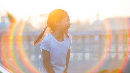 Cute asian child girl smiling with long hair outdoors in summer. Hair flare in the rays of the sunsetの写真素材