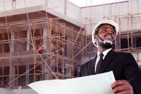 African site contractor engineer with hard hat holding blue print paper with building in backgroundの写真素材