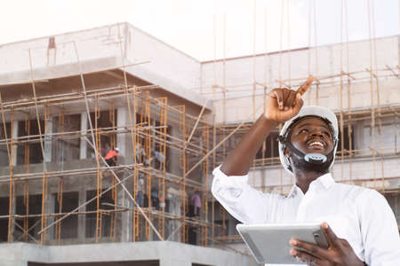 African site contractor engineer with hard hat holding tablet with the building in backgroundの写真素材