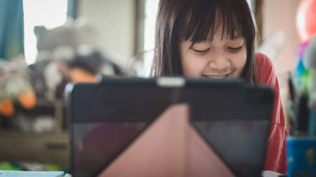 Asian little schoolgirl studying during her online lesson at home with smile and happy, social distance during quarantine,online education conceptの写真素材