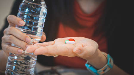 Woman taking medicine to cure disease with holding a bottle of waterの写真素材