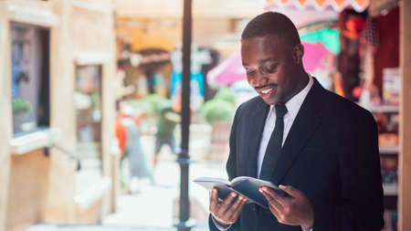 African man in a dark business suit in a white shirt looking in the book diary notebook standing in...