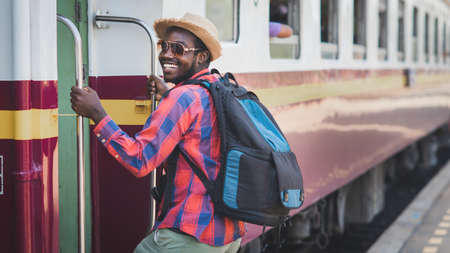African male traveler with hat and backpack entrain to the train on railway station.Adventure travel...