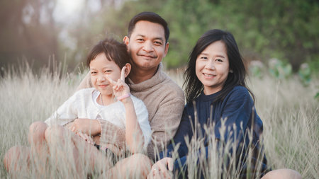 Happy family with father mother and daughter sitting and resting in park