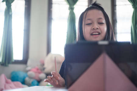 Asian little schoolgirl studying during her online lesson at home with smile and happy, social distance during quarantine,online education conceptの写真素材