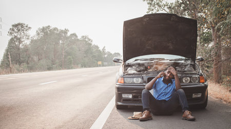 Stress african man calling for assistance or insurance with his car broken down by the roadsideの写真素材