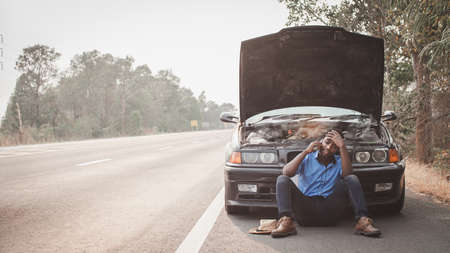 Stress african man calling for assistance or insurance with his car broken down by the roadsideの写真素材