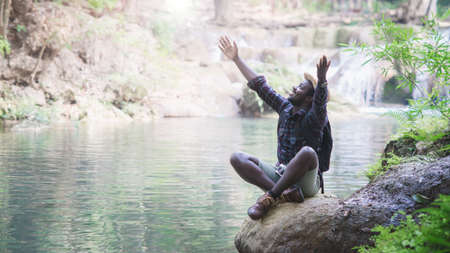 Freedom african man travel adventure with backpack and hat in forest and waterfall background. Travel conceptの写真素材