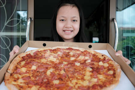 Asian little girl happily holds a large pizza delivery at homeの写真素材