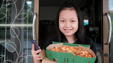Asian little girl happily to use smartphone and holding a pizza delivery at homeの写真素材