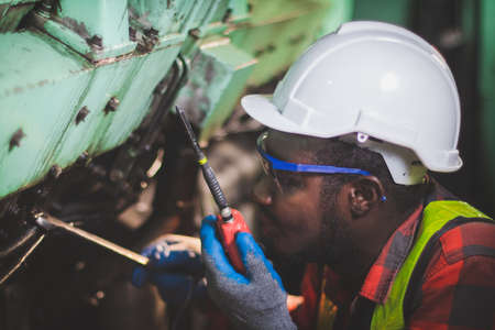 African man engineering engine machine controller checking, working and talking on radio communication to tell worker working in industryの写真素材
