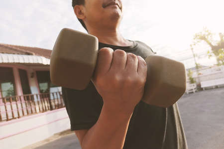 Strong asian man working out with heavy dumbbells  while covid-19 lockdown at homeの写真素材