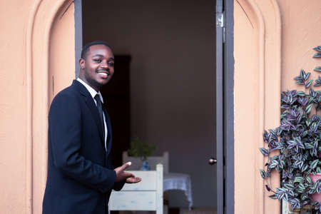 The restaurant and coffee shop owner is opening the door, inviting customers to his shop.Business african man standing and smilingの写真素材