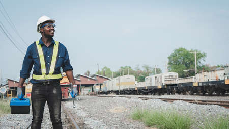 African machine engineer technician wearing a helmet, groves and safety vest is using a wrench to repair the trainの写真素材