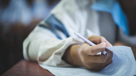 Students writing and reading exam answer sheets exercises in classroom of school with stressの写真素材