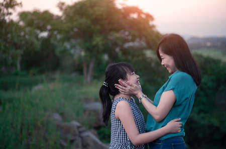 Mother and daughter are hugging and having fun outdoor in green nature with sunsetの写真素材