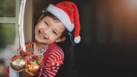 Concept of Christmas and child .The smiling girl stood behind the open door happily waiting to receive her Christmas presents.の写真素材