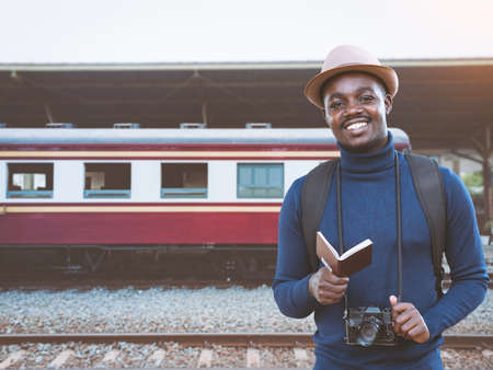 African male traveler with hat holding passport and waiting for the train on railway station.Adventure travel conceptの写真素材