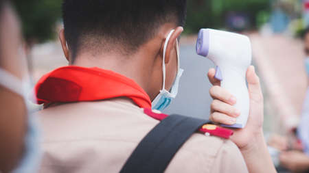 Teacher use infrared thermometer gun forehead temperature test to check student for protect virus covid-19 symptoms in the schoolの写真素材