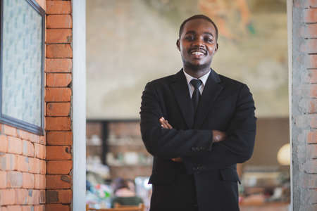 Portrait of elegant african businessman in black suit standing with crossing arms and smilingの写真素材