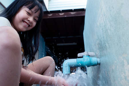 A young girl turns on the faucet to drink and use water with happy and smile.Concept of water and lifeの写真素材