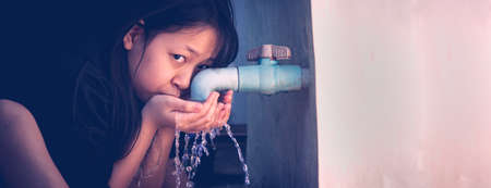 A poor girl turns on a drinking faucet and uses water with thirst.The concept of water and lifeの写真素材