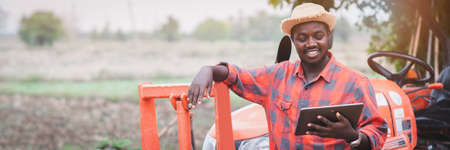 African man farmer working in the field with a tractor and using tabletの写真素材