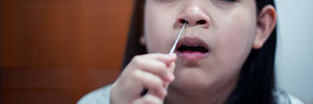 A young girl is swabing her nose to test for COVID-19 by herself with an ATK test kit