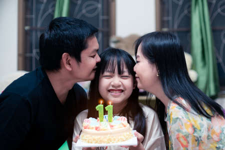 Happy parents kissing their daughter while blowing a birthday candle at homeの写真素材