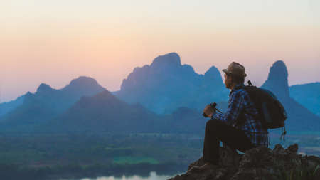 Hiker is sitting and looking sunset on top of mountain with packpack and holding the binoculars.Concept of adventure travelの写真素材