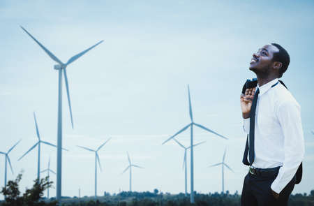 African businessman wearing a white shirt and standing happily, Relax, with a windmill in the...